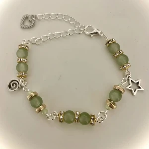Grönt armband med stjärndetalj - Charmigt armband med gröna pärlor och guldfärgade detaljer. Armbandet har en silverfärgad kedja med ett hjärtlås och en stjärnberlock. Perfekt för att ge en touch av elegans till din stil.