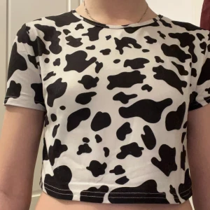 Svartvit croppad topp med koskinnsmönster - Säljer en cool croppad topp med svartvitt koskinnsmönster. Toppen har korta ärmar och en tight passform, perfekt för en trendig look. Passar bra till både jeans och kjol!