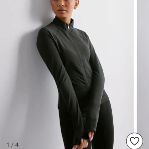 Svart träningsjacka från Nelly - Säljer en stilren svart jacka med dragkedja. Jackan har en tight passform och är långärmad, perfekt för träning eller som ett lättare lager. Materialet är syntetiskt och ger en smidig känsla. Perfekt för dig som vill ha en enkel och funktionell jacka.