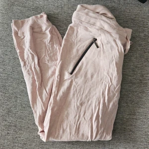 Rosa mjukisbyxor med dragkedja - Säljer ett par bekväma rosa mjukisbyxor med dragkedja på sidan. Perfekta för en avslappnad dag hemma eller på språng. Byxorna har en elastisk midja för extra komfort.