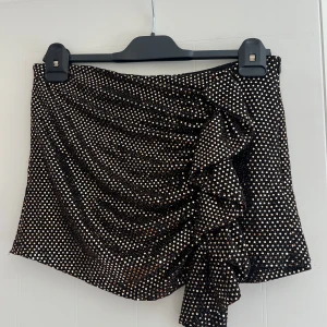Svart glittrig guld kjol från Zara - Snygg svart & guldig shorts-kjol från Zara med volangdetalj fram. Det är shorts där bak men framtill ser det ut som en vanlig kjol! Nypris 379kr