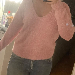 Rosa fluffig tröja - Mysig rosa tröja med fluffig textur och v-ringad hals. Perfekt för att hålla sig varm och stilren under kyligare dagar. Långärmad design som ger en bekväm passform.