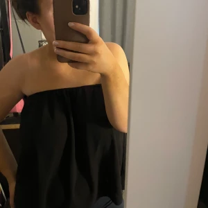 Svart axelbandslös topp - Säljer en stilren svart axelbandslös topp. Toppen har en luftig passform och är lätt att matcha med olika outfits. Går också att använda som kjol!