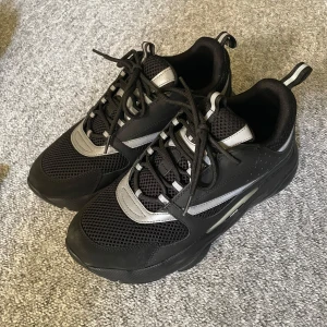 Svarta sneakers från HM - Snygga svarta sneakers från hm med grå detaljer och snörning. Skorna har en sportig design med mesh och syntetmaterial för en modern look. Perfekta för en stilren vardagsstil. Skorna är smutsiga.