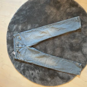 Ljusblå jeans från Levi's W31 L32 - Säljer ett par klassiska ljusblå Levi's jeans. De har en straight passform och är tillverkade i jeansmaterial. Perfekta för en avslappnad stil. Levi's ikoniska lädermärke syns på baksidan.
