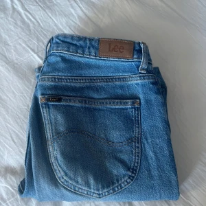 Blå jeans från Lee - Snygga blå jeans från Lee med klassisk femficksdesign och en bekväm passform. Perfekta för en avslappnad stil. De har en traditionell Lee-logga på baksidan och en dragkedja framtill.