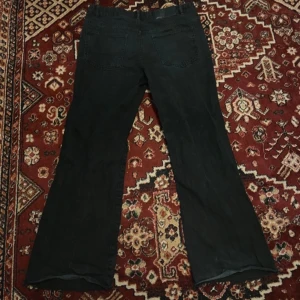 Bootcut jeans - Snygga svarta jeansbyxor med en klassisk design. Byxorna har en boot cut passform och är perfekta för en stilren look. De har bakfickor och en knappgylf framtill.