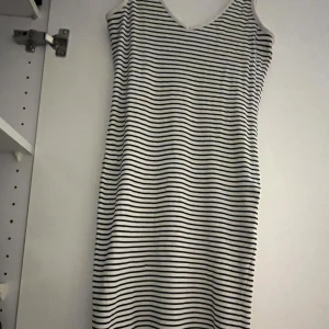 Randig ärmlös klänning - Säljer en stilren ärmlös klänning med svarta och vita ränder. Klänningen har en v-ringad hals och är gjord i ett ribbat material som ger en skön passform. Perfekt för en avslappnad look!