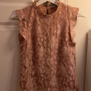 Rosa spetsblus - Säljer en romantisk rosa spetsblus med vackra blommönster. Blusen är ärmlös och har volangdetaljer vid axlarna. Perfekt för en somrig look! Fråga vid funderingar!!❤️
