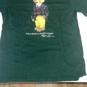T-shirt med Polo Bear från Ralph Lauren - Säljer tre olika t-shirts från Ralph Lauren med det ikoniska Polo Bear-motivet. En mörkblå, en grön och en flerfärgad med korta ärmar. Perfekta för en avslappnad stil med en touch av lyx.