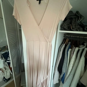 Ljusrosa omlottklänning - Säljer en elegant ljusrosa omlottklänning med korta ärmar och v-ringning. Perfekt för en stilren look.