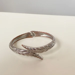 Silverfärgat armband med vriden design - Snyggt vintage silverfärgat armband med en unik vriden design. Armbandet har en slät yta med subtila detaljer som ger det en modern och stilren look. Perfekt för att ge din outfit en extra touch av elegans. Lite tecken på användning finns, men syns knappt 