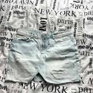 Ljusa jeansshorts från Zara - Säljer ett par ljusa jeansshorts från Zara med slitna detaljer och fransar. Shortsen har en knapp och dragkedja framtill samt klassisk femficksdesign. Perfekta för en avslappnad stil.