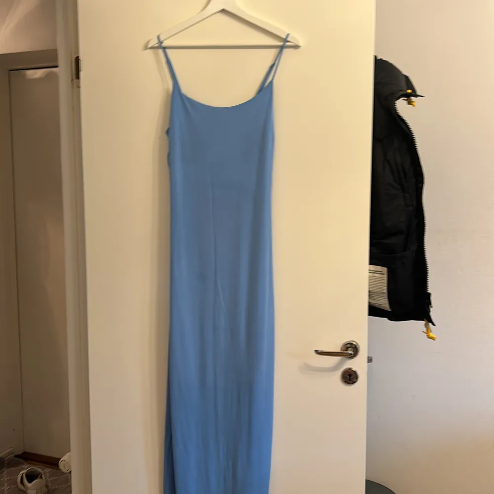 Säljer en stilren blå långklänning från Bik Bok. Klänningen har smala axelband och en enkel design som gör den perfekt för olika tillfällen. Materialet känns mjukt och bekvämt mot huden. Perfekt för dig som vill ha en elegant och minimalistisk look.. Mekot.