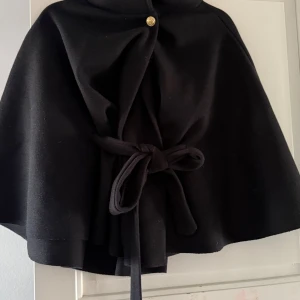 Svart poncho jacka  från Missay - Snygg svart cape från Missay med knytband i midjan och en guldig knapp framtill. Aldrig använd och i ett ny skick! 