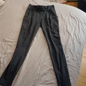 Svarta ridbyxor från Copperfield - Snygga svarta ridbyxor från Copperfield i storlek 150. Byxorna är tillverkade av 78% polyester och 22% spandex, vilket ger en stretchig och bekväm passform. Perfekta för ridning med en stilren design.