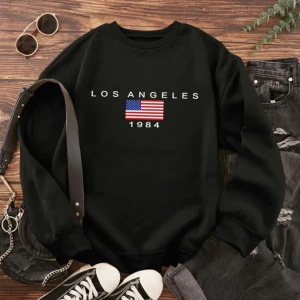 Svart sweatshirt med tryck - Säljer en svart sweatshirt med texten 'Los Angeles 1984' och en amerikansk flagga på framsidan. Tröjan har långa ärmar och en rund halsringning. Perfekt för en avslappnad stil.