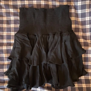 Svart volangkjol - Snygg svart kortkjol med volanger. Perfekt för att ge en trendig touch till din outfit. Den har en elastisk midja för en bekväm passform. Passar bra till både vardagliga och mer uppklädda tillfällen.