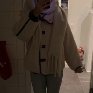 Beige teddyjacka med svarta detaljer - Mysig beige teddyjacka med svarta detaljer och knappar. Perfekt för kyliga dagar med sin fluffiga och varma design. Jackan har långa ärmar och en avslappnad passform. Från hm, inte jätte använd 💕💕💕