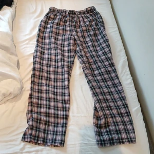 Rutiga mjukisbyxor i bomull - Säljer ett par rutiga mjukisbyxor med elastisk midja. Byxorna har ett klassiskt rutmönster i svart, rosa och vitt och är gjorda i mjuk bomull. Perfekta för chill dagar hemma eller när du vill vara extra bekväm.