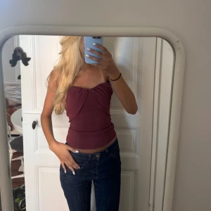 Vinröd tubtopp med snygg drapering - Säljer en vinröd tubtopp med snygg drapering framtill. Toppen är figurnära och axelbandslös, perfekt för dig som gillar en clean och trendig look. 