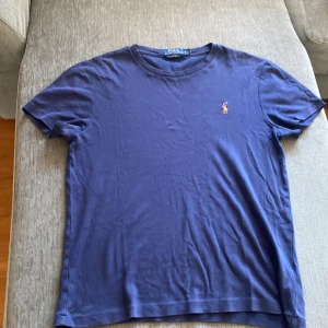 Blå Polo Ralph Lauren t-shirt slim fit - Snygg blå t-shirt från Polo Ralph Lauren i bomull med klassisk broderad logga på bröstet. Modellen är custom slim fit och har korta ärmar och rund hals. Perfekt för dig som gillar stilrena och tidlösa plagg med premiumkänsla.