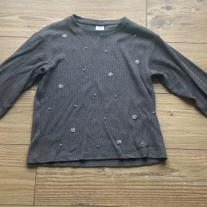 Grå ribbad tröja med pärlor från Zara - Grå långärmad tröja från Zara med ribbad struktur och dekorativa pärlor och små blommor framtill.         3 av pärlorna har lossnat men det är inget som syns. Använd men tvättar 2 gånger innan de skickas.
