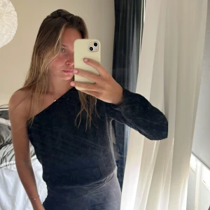 Svart stickad oneshoulder-tröja - Svart stickad tröja med oneshoulder-design och lång ärm. Snygg ribbad struktur som ger en stilren look. Perfekt för dig som vill ha något trendigt och bekvämt med en twist. Passar till både jeans och kjol.