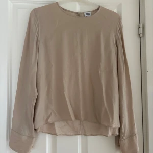 Beige blus från Twist & Tango - Säljer en stilren beige blus från Twist & Tango i storlek 38. Blusen har långa ärmar med snygga manschetter och knappar i guldton. Den är tillverkad i ett tunt, mjukt material med rund halsringning och diskret knapp bak i nacken.