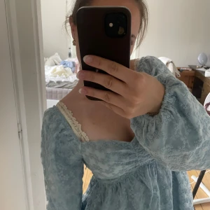 Ljusblå puffärm klänning i spets - Supersöt ljusblå kort klänning från NA-KD med puffiga långa ärmar och spetsdetaljer. Klänningen har en romantisk känsla med broderat blommönster och markerad midja. Perfekt för dig som gillar en feminin och trendig stil.