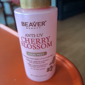 Beaver Beauty Cherry Blossom Hair Mist - Säljer en rosa hårmist från Beaver Beauty med doft av körsbärsblom. Anti-UV-formula som skyddar håret mot solens strålar och föroreningar. Ger elasticitet, styrka och glans. Kommer i en smidig sprayflaska på 80 ml med guldfärgat lock.