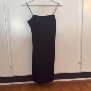 Svart långklänning från NA-KD - En stilren svart långklänning från NA-KD med smala axelband och rak passform. Klänningen är enkel och elegant, perfekt för dig som gillar minimalistisk stil. 
