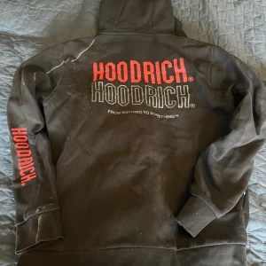 Svart hoodie från Hoodrich med tryck - Svart hoodie från Hoodrich med stor logga i rött och vitt på ryggen, samt tryck på bröstet och ena ärmen. Klassisk huva med snörning och känguruficka framtill. Perfekt streetwear-vibe och riktigt skön passform. Viss missfärgning som jag ej provat få bort. Ett helt set svart med beige text på både byxa och hoodie. Båda hoddiesen är skavda på vänster armbåge (se bilder). En hål i en byxfickan men inget som syns och kan lätt lagas för den händige.