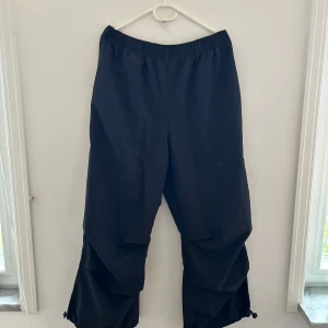 Svarta wide parachute pants med snörning - Svarta parachute pants  med bred passform och elastisk midja. Byxorna har dragsko längst ner vid bensluten för att justera passformen. Lösa och sköna! 
