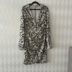 Zebramönstrad kortklänning H&M - Snygg kortklänning från H&M med zebramönster i svart och vitt. Klänningen har lång ärm, v-ringning och cool rynkdetalj framtill. Perfekt för dig som vill sticka ut med ett djurmönster och trendig look.