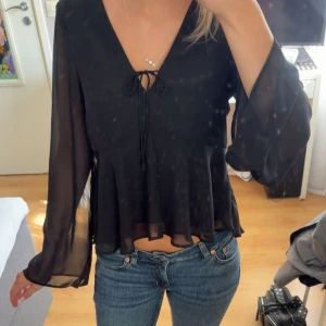 Svart blus - Säljer en svart blus med v-ringning och knyt framtill. Blusen har långa, vida ärmar i transparent och tunt material som luftar bra. Super vacker inför evenemang där man måste klä upp sig. Använd fåtal gånger. Tveka inte att fråga om du undrar något! 💌