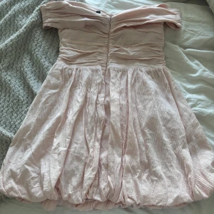 Ljusrosa offshoulder kortklänning - Supersöt ljusrosa kortklänning med offshoulder och rynkade detaljer upptill. Kjolen är puffig och har en ballongliknande form. Perfekt för sommarens alla tillfällen och ger en romantisk vibe.