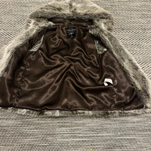 Grå pälsjacka från Atmosphere - Säljer en fluffig och snygg grå pälsjacka från Atmosphere. Jackan har ett lyxigt foder i brunt satinliknande material och en cool mix av gråa och vita nyanser i pälsen. Perfekt för dig som vill sticka ut och hålla dig varm under kalla dagar.