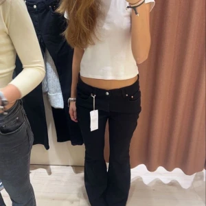 Svarta bootcut jeans låg midja - Säljer ett par svarta jeans med låg midja och bootcut-silhuett. Jeansen har klassisk femficksdesign och är i ett stretchigt bomullsmaterial som sitter snyggt på kroppen. Perfekta för dig som gillar en retro vibe och vill ha en smickrande passform.