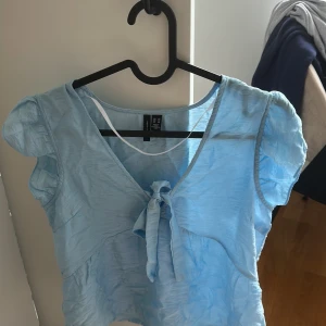 Ljusblå blus med knyt från Vero Moda - Supersöt ljusblå blus från Vero Moda med puffiga korta ärmar, v-ringning och knyt framtill. Aldrig använd köpt ganska nydligen. Ganska skrynklig men går att stryka