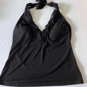 Svart halterneck linne vintage - Snyggt svart linne med halterneck och knyt i nacken. Toppen har en djup v-ringning med dekorativa virkade detaljer längs kanten. Köpt vintage i New York. 