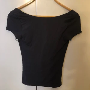 Grå topp med öppen rygg - Säljer denna super snygga t-shirten med öppen rygg då den inte kommer till användning, den ser nästan ut som svart på bilderna men den är mörk grå, använt fåtal gånger så den är som ny! Priset kan diskuteras ☺️