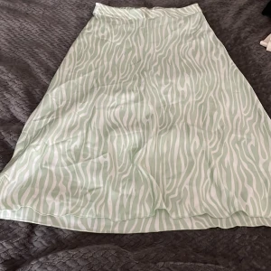 Mintgrön zebramönstrad långkjol Vero Moda - Snygg långkjol från Vero Moda i mintgrönt och vitt zebramönster. Kjolen har en flowy passform och resår i midjan för extra komfort. Perfekt för dig som vill sticka ut med ett coolt mönster och mjukt, glansigt material.