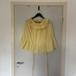 Gul volangkjol från Chana by Bel - Supersöt ljusgul kortkjol med volanger och bred resår i midjan från Chana by Bel. Kjolen har knytband och en romantisk volangkant upptill som ger en lekfull vibe. Perfekt för dig som gillar en feminin och trendig look.