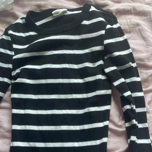 Svartvit randig långärmad tröja - Snygg svart långärmad tröja med vita horisontella ränder. Tröjan har en klassisk rund halsringning och är gjord i ett mjukt, ribbat material som sitter skönt mot kroppen. Perfekt för dig som gillar en enkel men stilren look.