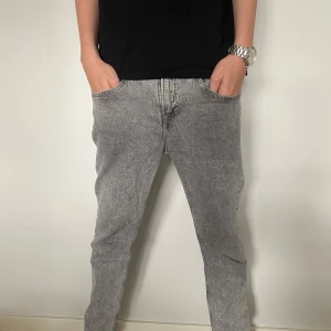 Grå slim fit jeans från &Denim - Säljer ett par grå slim fit jeans från &Denim. Jeansen har en snygg tvättad look, klassiska femficksdetaljer och raka ben. Perfekta för dig som gillar en stilren och avslappnad vibe. Materialet är mjukt denim som sitter skönt hela dagen.