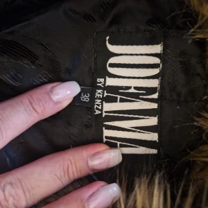 Svart skinnjacka Jofama by Kenza - Snygg svart skinnjacka från Jofama by Kenza med stor, fluffig fuskpäls i kragen. Jackan har dragkedjor på ärmar och fickor samt coola detaljer som ger en edgy vibe. Perfekt för dig som vill sticka ut med en statementjacka.