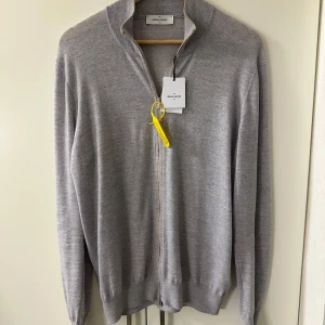 Ljusgrå kofta från Gran Sasso - Snygg ljusgrå kofta från Gran Sasso med hel dragkedja. Tillverkad i mjuk virgin ull som känns lyxig mot huden. Perfekt för lager-på-lager och har en clean, stilren look. Passformen är normal och ärmarna dessutom. Tröjan är helt ny och kvitto finns kvar som skickas med vid köp. Nypris 3500 mitt pris är endast 799! Först till kvarn