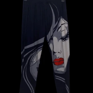 Svarta/Marinblåa leggings med ansiktsmönster - Unika svarta/marinblåa leggings med ett stort grafiskt ansikte i grått och vitt samt röda läppar på framsidan. Mjukt och stretchigt material med resår i midjan. Perfekta för dig som vill sticka ut med en cool och konstnärlig look.
