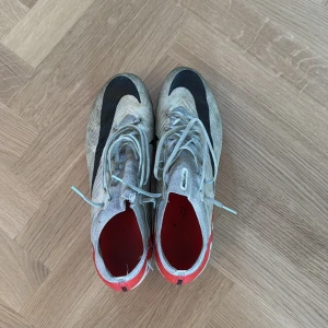 Nike Air Zoom fotbollsskor röd/vit - Nike Air Zoom fotbollsskor med snygg design i vitt, rött och svart. Ovandel i syntetmaterial med svart swoosh och röda detaljer. Skorna har snörning och dobbar för bästa grepp på planen. Perfekta för dig som vill ha lätta och snabba skor till matchen. Ag dobbar